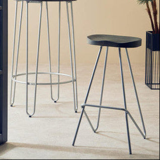 Two black stools with thin legs in a room with a beige wall and a plant.