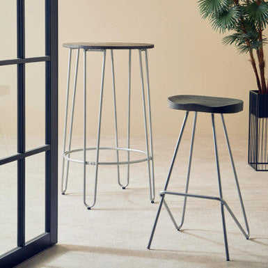 Two black stools with thin legs in a room with a beige wall and a plant.