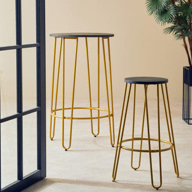Two gold metal bar stools with black seats in a room with a plant and window.