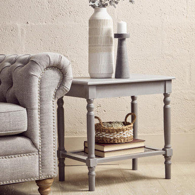 Light gray side table with decorative items next to a gray sofa against a beige wall.