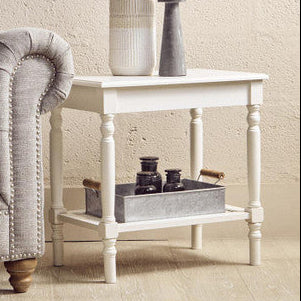 Gray tufted sofa next to a white side table with decorative items against a beige wall.