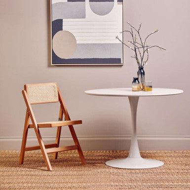 Modern interior with a white round table, wooden chair, and abstract art on the wall.