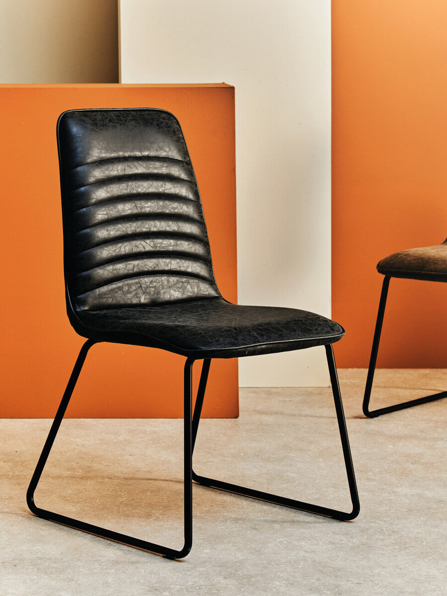 Black chair with ribbed backrest against an orange and white wall.