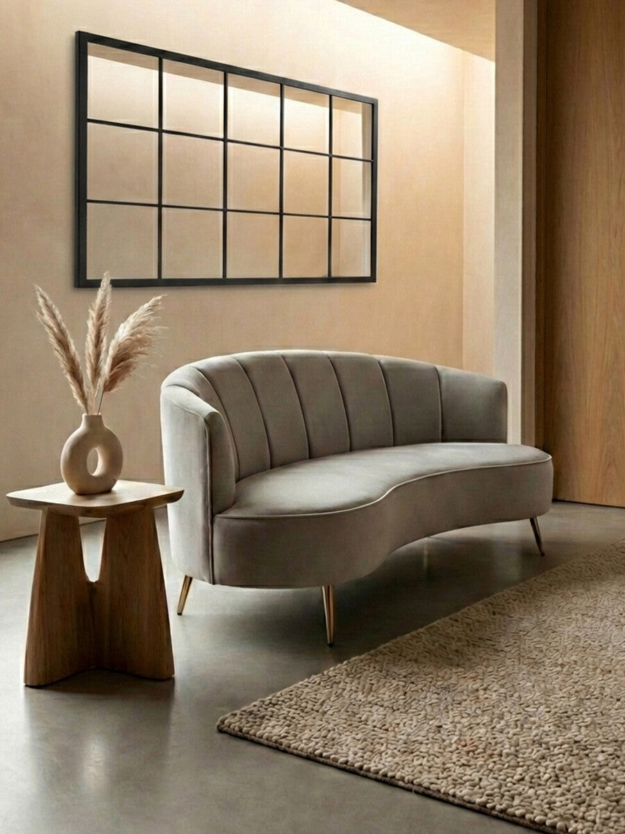 Modern living room with a curved gray sofa, wooden side table, and decorative mirror.