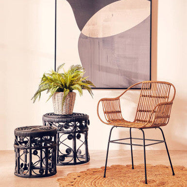 Wicker chair and stools with a plant in a room with abstract art on the wall.