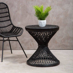 Black woven side table with a plant next to a black chair against a gray wall.