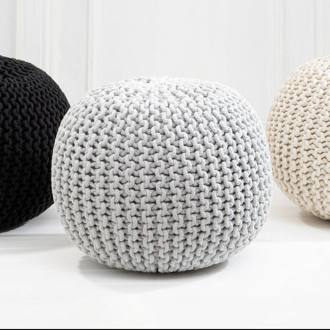 Three knitted poufs in black, white, and gray on a light wooden floor.
