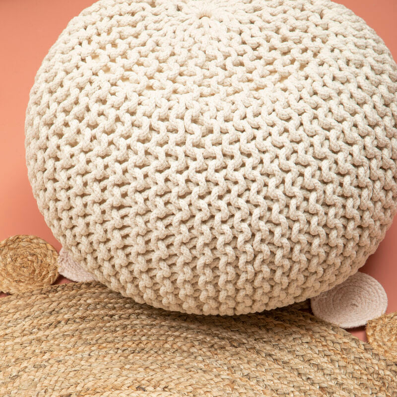 Knitted beige pouf on a matching woven rug against a pink wall