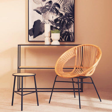 Wicker chair and stool with a black and white plant-themed painting on a beige wall.