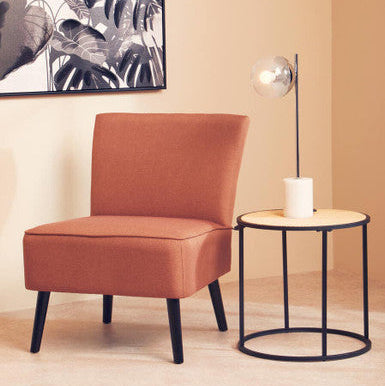 Orange chair and black side table with a candle in a room with a plant-themed wall art.
