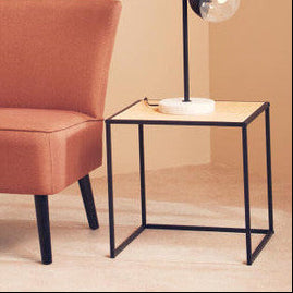 Orange chair and side table with a lamp in a room with a leafy artwork on the wall.