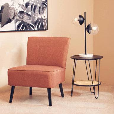 Orange chair and black side table against a beige wall with a leafy artwork.