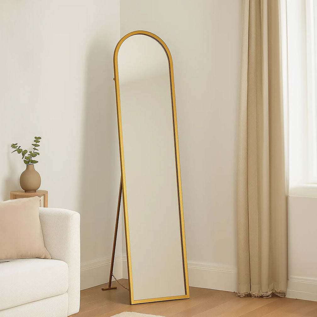 Gold-framed standing mirror in a room with a white sofa and a small plant.