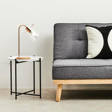 Gray sofa with wooden legs in a minimalistic room with a side table and lamp.