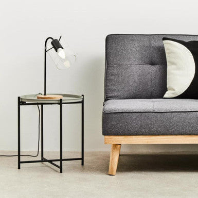 Gray sofa with wooden legs and a side table with a lamp in a minimalistic room.