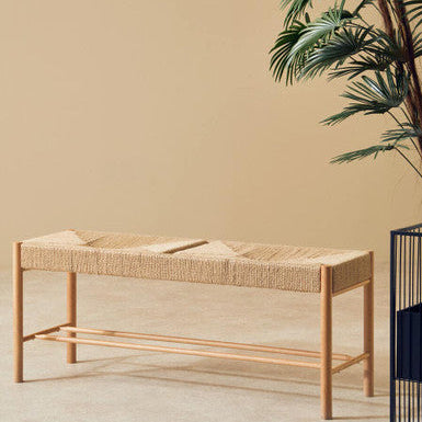 Woven bench against a beige wall with a plant on the right side