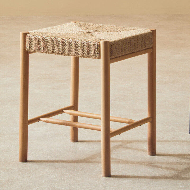 Wooden stool with woven seat next to a black metal plant stand on a beige floor.