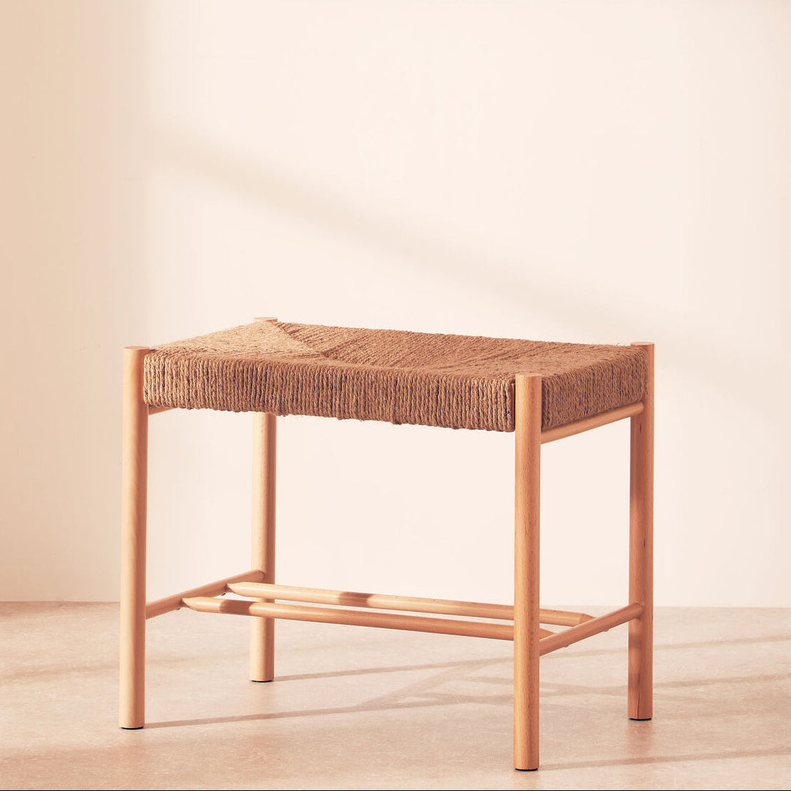 Small stool with woven top and wooden frame on a light wooden floor.