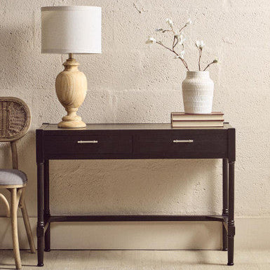 Dark wooden console table with a lamp, books, and vase against a beige wall.