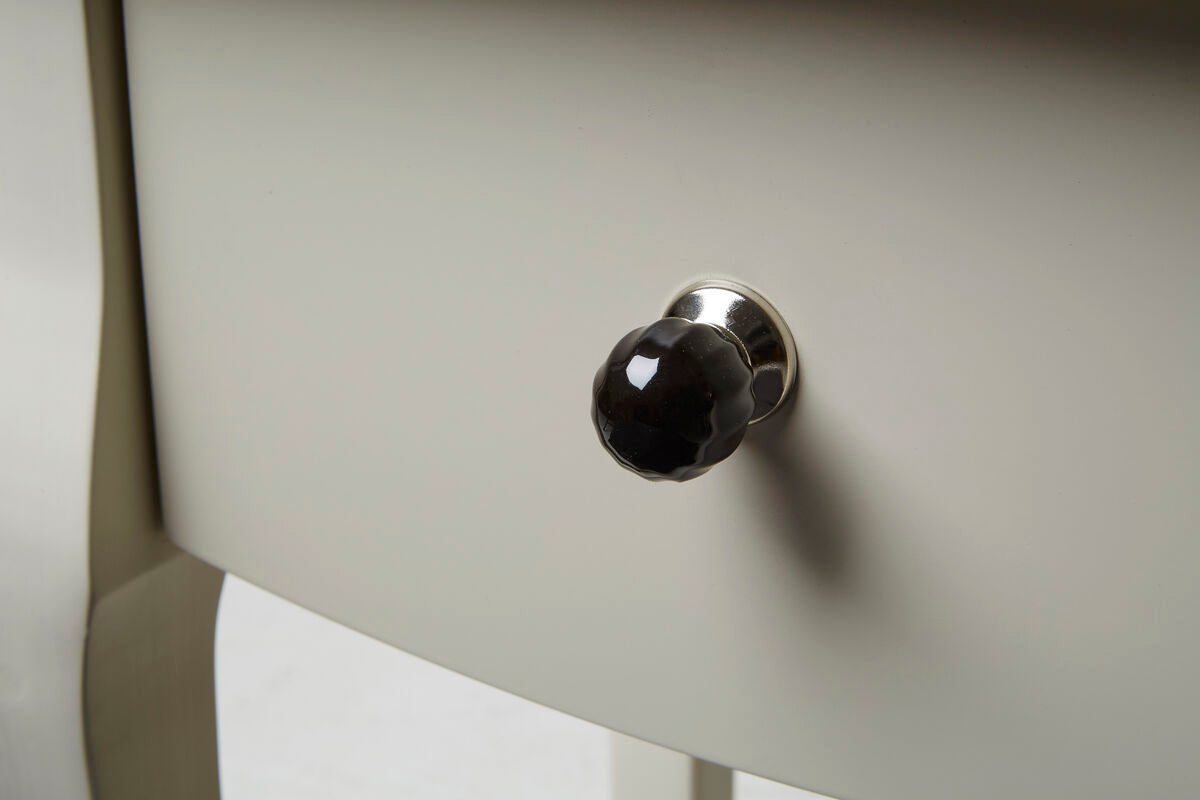 Close-up of a black knob on a light-colored cabinet door.