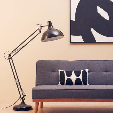 Gray sofa with a black and white pillow, black floor lamp, and abstract art on a beige wall.