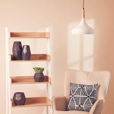 Beige armchair with a patterned pillow next to a wooden shelf against a beige wall.