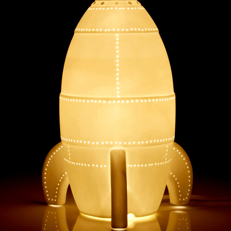 Rocket-shaped lamp with a warm glow on a reflective surface against a black background