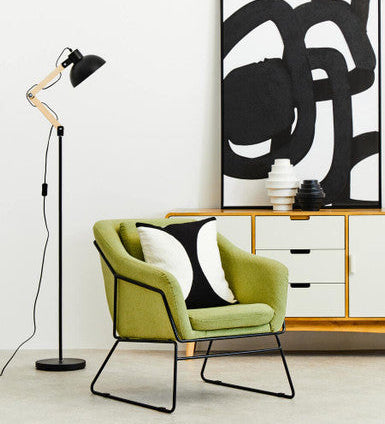 Modern interior with a green chair, black floor lamp, and abstract art on a white wall.