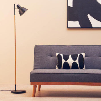 Gray sofa with a black and white pillow, standing lamp, and abstract wall art in a room.