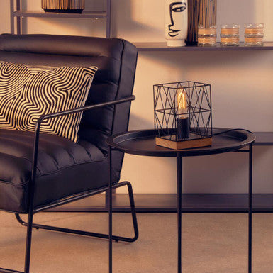 Modern living room with a black armchair, side table, and decorative items.