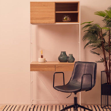 Modern office setup with a wooden desk, chair, and shelves against a light pink wall.