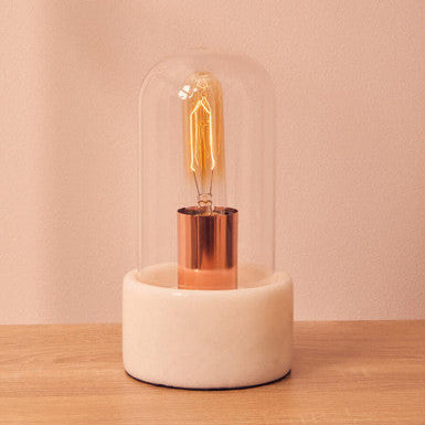 Vintage-style light bulb in a glass dome on a wooden surface with a pinkish-beige background