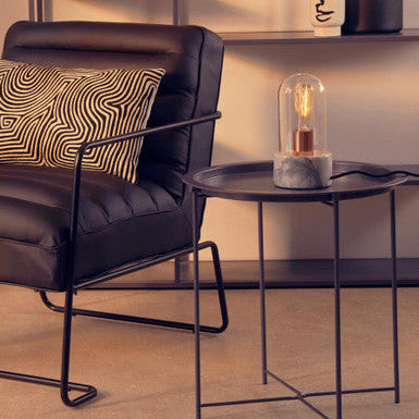 Modern black leather armchair with a side table featuring a decorative light bulb in a room setting.