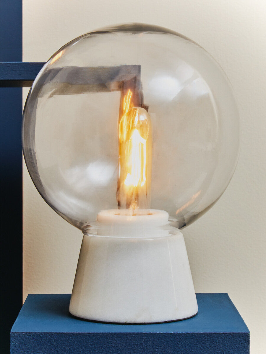 Table lamp with a clear glass shade and white base on a blue surface.
