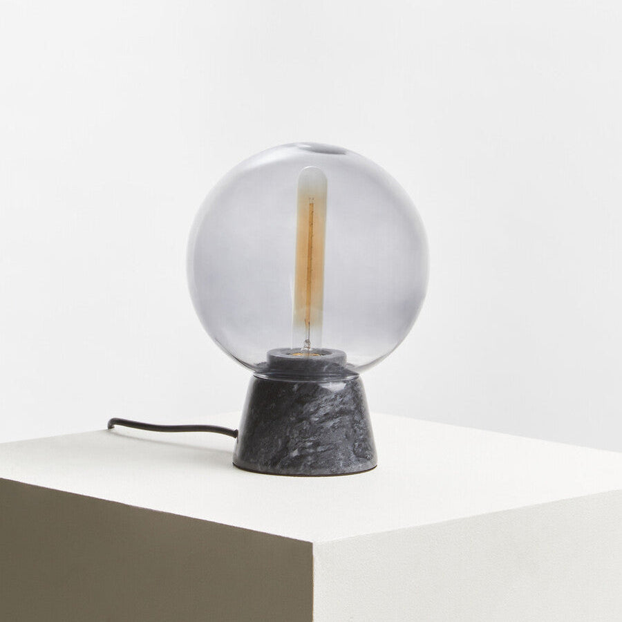 Table lamp with a clear glass shade and black marble base on a white surface.