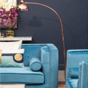 Blue armchair with decorative pillows in a room with a tall floor lamp and purple flowers.