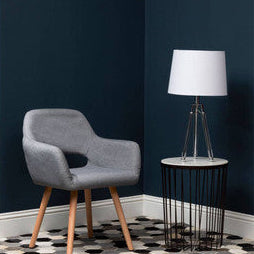 Gray chair with wooden legs next to a lamp on a patterned rug in a room with dark blue walls.
