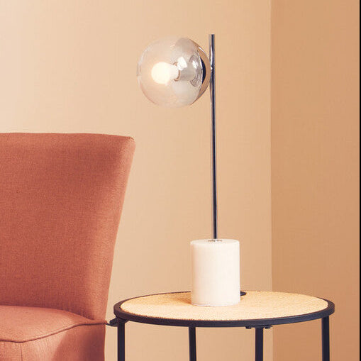 Orange chair and black side table against a beige wall with a framed leaf print.