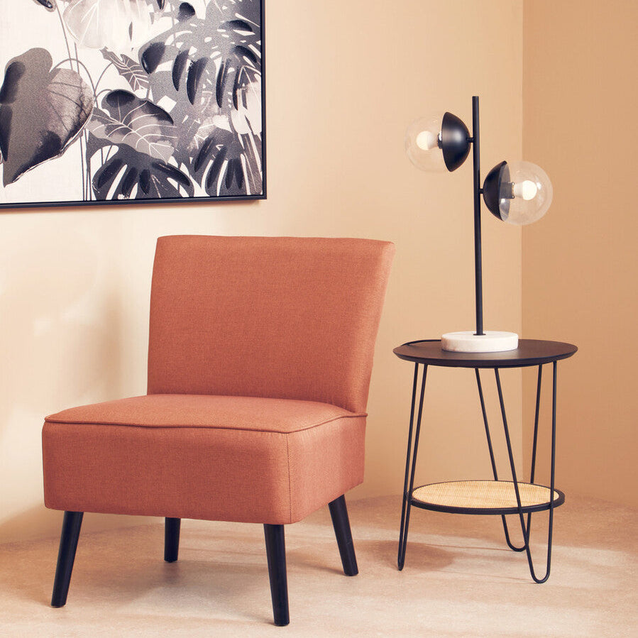 Orange chair and black side table against a beige wall with a leafy artwork.