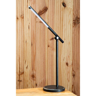 Black adjustable desk lamp on a wooden surface with a wooden panel background