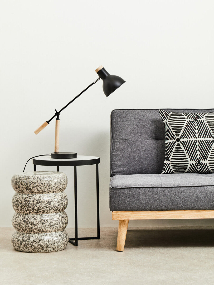Gray sofa with a decorative pillow, black lamp, and textured side table in a minimalistic room.