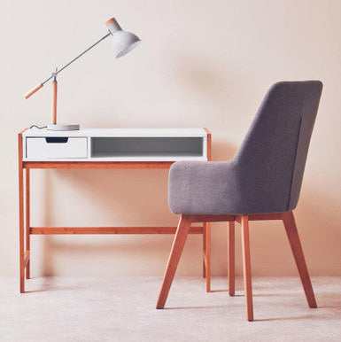 Minimalist desk setup with a chair and lamp against a plain wall.