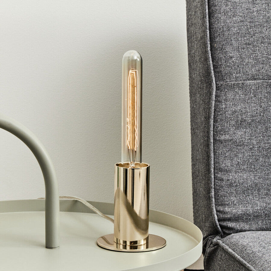 Modern table lamp with gold base on a side table next to a gray armchair.