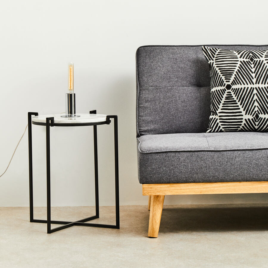 Gray sofa with a geometric-patterned pillow next to a small side table in a minimalistic room.