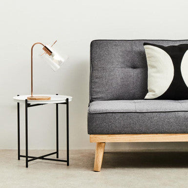 Gray sofa with wooden legs in a minimalistic room with a side table and lamp.