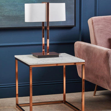Modern side table with marble top and copper frame in a stylish room.