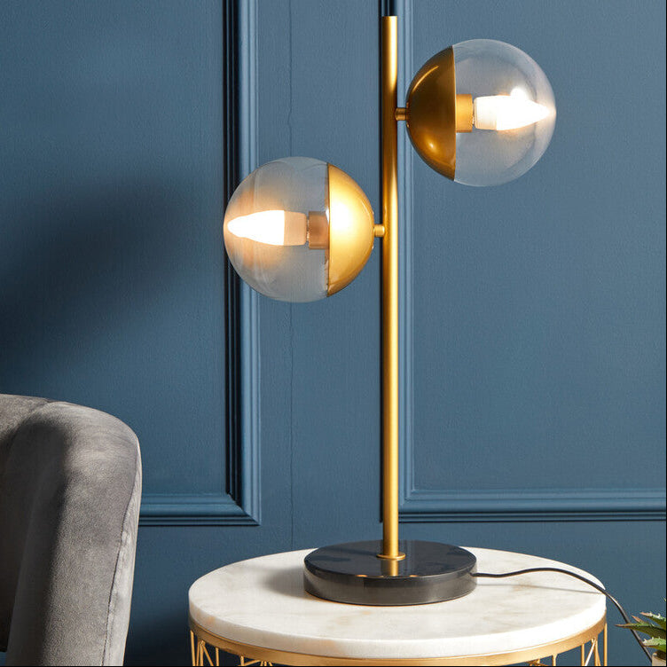 Modern table lamp with gold finish and glass shades on a marble side table against a blue wall.