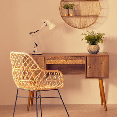 Wooden desk with wicker chair and round wall shelf in a room.