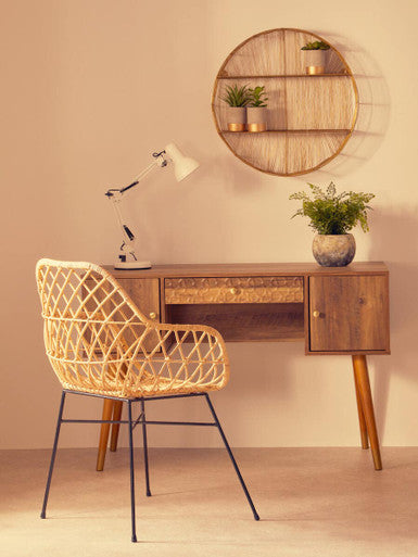 Wooden desk with wicker chair and round wall shelf in a room.