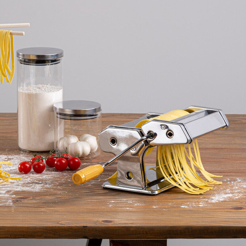 Pasta maker on a wooden table with ingredients and pasta strands.